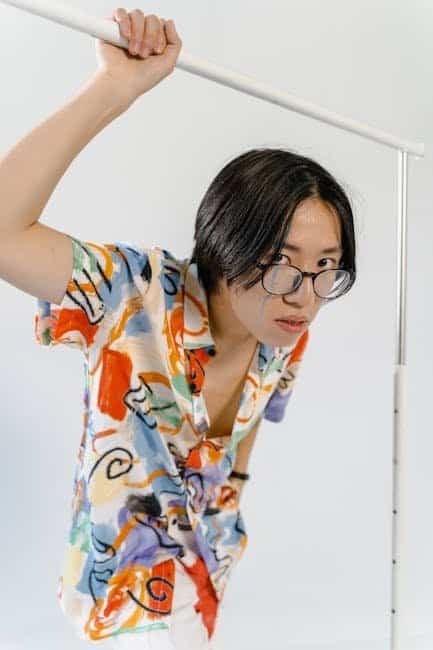 Exploring The Cool Shirt Shop: Unique Finds for the Fashion-Forward Person holding a white pole wearing a colorful patterned shirt and glasses.