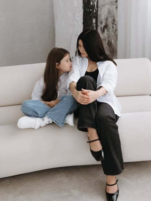 Mother and daughter sitting on a white sofa, engaging in a heartfelt moment.