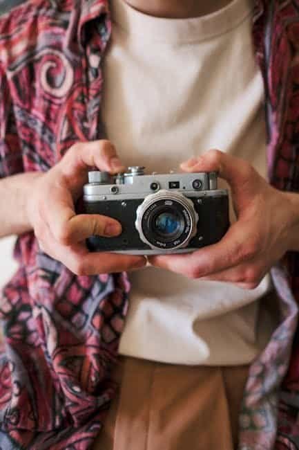 The Cool Shirt Shop: Where Art Meets Fashion Person holding a vintage camera with a patterned shirt and beige pants.