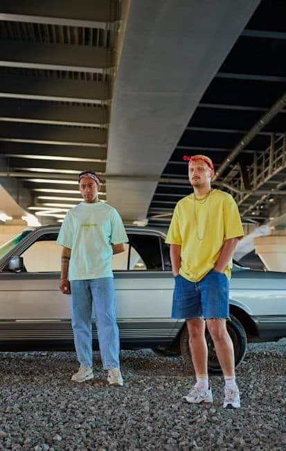 The Role of Accessories in Men's Fashion: When to Stand Out or Blend In Two young men in casual clothes standing by a car under a bridge at sunset.