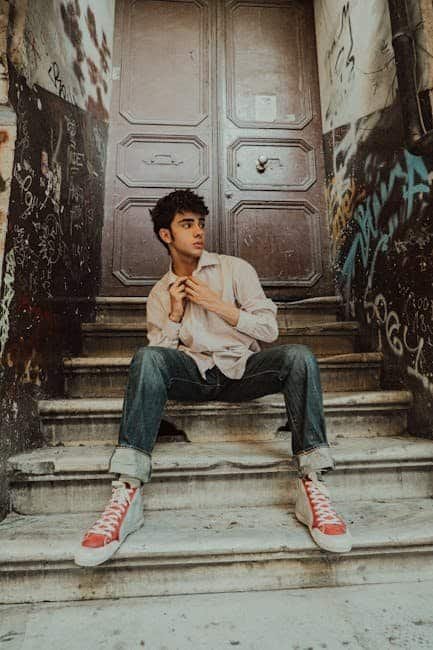 The Cool Shirt Shop: A Revolution in Men's Fashion Young man in casual clothes sitting on graffiti-covered stairs near a large door.