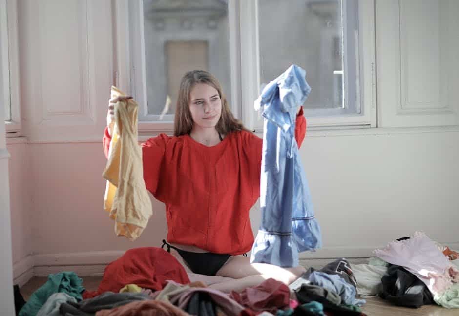 Young woman folding clothes with laundry scattered around in a bright room.